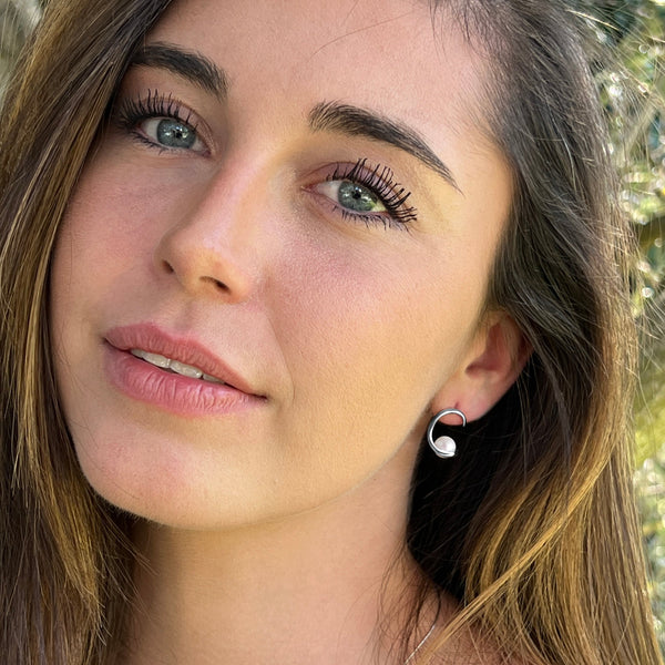 Boucles d’oreilles Calliopé portées en argent 925, design ouvert en forme de croissant enveloppant une perle de culture d’eau douce blanche.