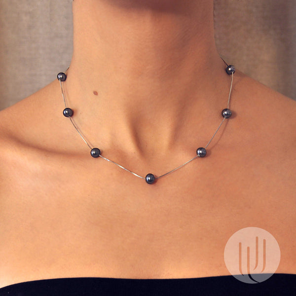 Vue portée sur mannequin d’un collier composé de 9 perles noires taille 7mm semi rondes alignées sur une chaîne en argent 925, d’une longueur de 45 cm.