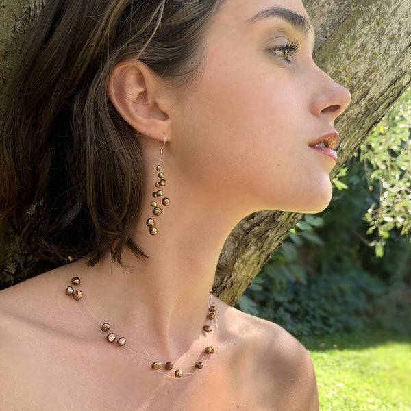 Ensemble Constellation porté, composé d’un collier et de boucles en perles de culture d’eau douce dorées montées sur fil de nylon et argent 925.